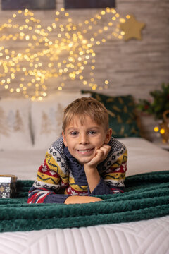 Cute preschool boy, sitting in front of the fireplace, holding christmas present and reading a book, joy and happiness