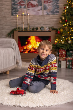Cute preschool boy, sitting in front of the fireplace, holding christmas present and reading a book, joy and happiness