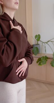Vertical video: Woman on purple mat, placing hands on chest and belly, breathing to relax in hoodie