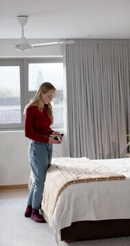 Vertical video: Woman 20s red top fixing tangled cord touching knit testing black phone bud by bed