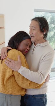 Vertical video: Pair with woman leaning in while Senior Asian man holding and comforting by window