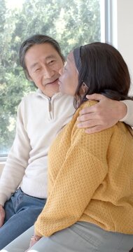 Vertical video: Diverse duo, woman moving closer and leaning into senior man showing care at window