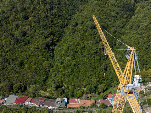 Aerial view of a large yellow construction crane positioned near a row of small houses with red roofs, set against a dense green forest hillside in Istanbul, Istanbul, Turkiye.