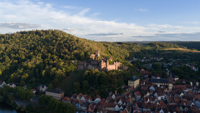 Aerial view of Wertheim Castle perched on a forested hill overlooking the historic town rooftops and the river valley during the golden hour in Wertheim, Baden-Wurttemberg, Germany.