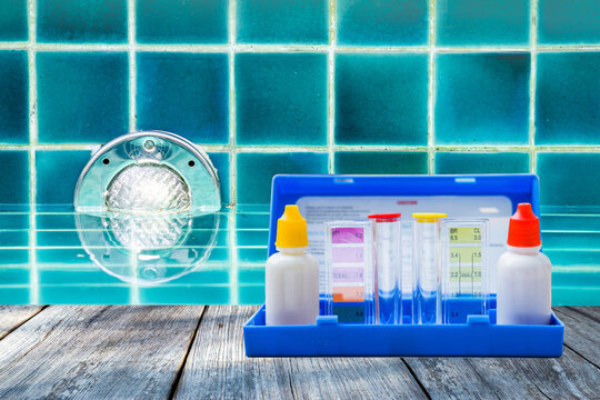 Swimming pool water tester test kit on wooden table over swimming pool wall lamp background, pool service and maintenance industry, quality water test