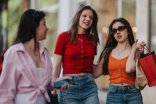 Three young women walk together carrying shopping bags and chatting. Candid street photo of friends enjoying a casual shopping outing in the city.