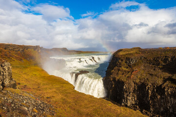 Beautiful panoramic view of powerful Gullfoss waterfall cascades with a bright rainbow under dramatic stormy clouds, Iceland © olyasolod