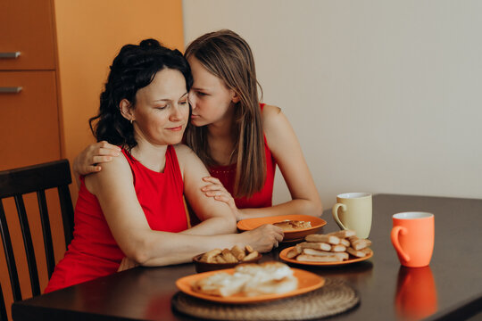 Two women embrace at kitchen table while one appears emotional creating intimate support scene connected with empathy female friendship mental wellness compassionate care trust and human connection.