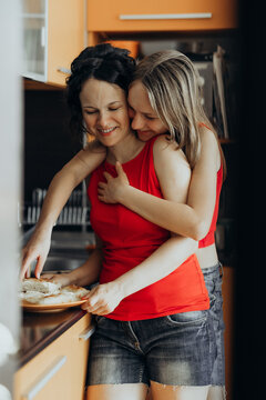Two women smile while preparing food together in home kitchen creating joyful lifestyle scene about shared cooking friendship bonding social wellbeing collaborative routines and everyday happiness.