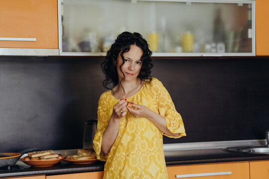 Smiling woman in yellow dress enjoys small bite beside prepared food in modern kitchen creating lifestyle scene around mindful eating home comfort balanced routines self care and intentional living.