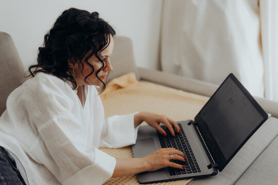 Curly haired woman works on laptop from comfortable home setting creating remote work scene linked with flexible employment digital productivity hybrid careers career autonomy and modern workforce.