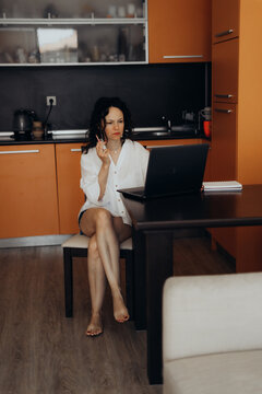 Woman sits at dining table using laptop with hand near face creating remote communication scene linked with virtual meetings entrepreneurship digital business smart decision making and flexible work.