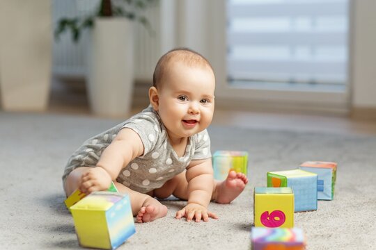 Happy baby crawling and reaching for colorful blocks indoors