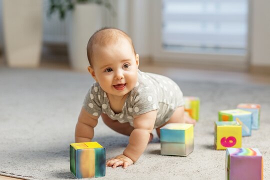 Happy baby crawling toward colorful building blocks indoors