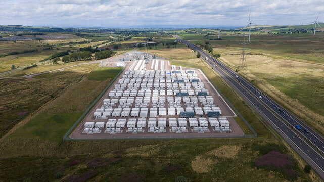 Aerial view of the Coalburn Battery Energy Storage System with rows of white battery containers and a substation next to a highway in the rural landscape of Coalburn, Scotland, United Kingdom.