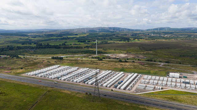Aerial view of the large-scale battery energy storage system in Coalburn, featuring rows of white containers, wind turbines, and rolling green hills, Coalburn, Scotland, United Kingdom.