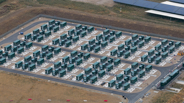 Aerial view of a large-scale battery energy storage system with rows of green containers on concrete pads, surrounded by gravel paths in London, England, United Kingdom.