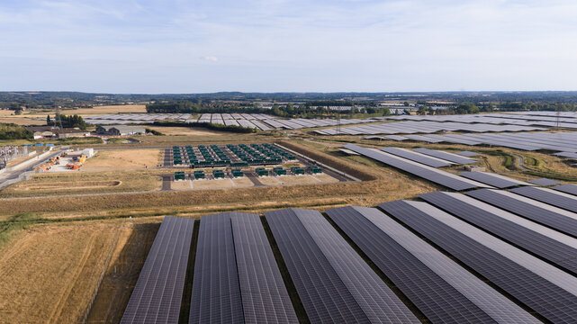 Aerial view of a large-scale solar farm featuring rows of photovoltaic panels and a central battery energy storage system in the rural landscape of London, England, United Kingdom.