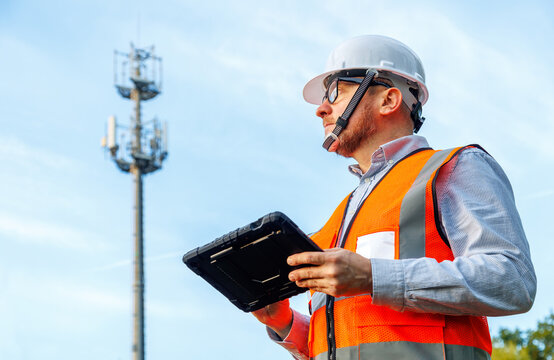 Engineer running AI network optimisation, automated inspection, and site control. Telecom technician using AI mobile application on tablet in protective case near 5G cell tower. 