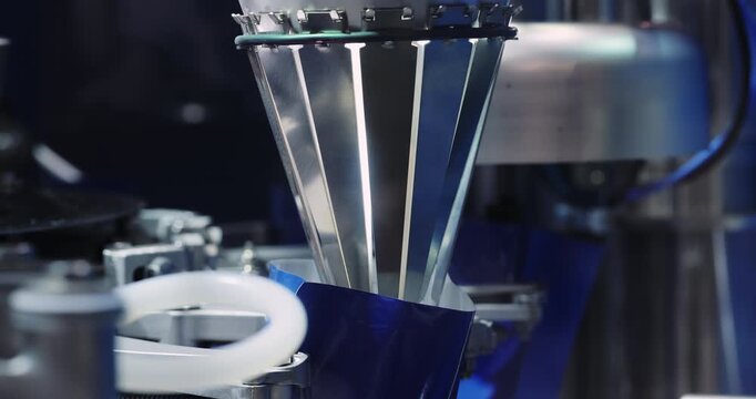 Industrial filling heads dispense cosmetic product into containers on automated line. Precision machinery controls flow supporting consistent factory output