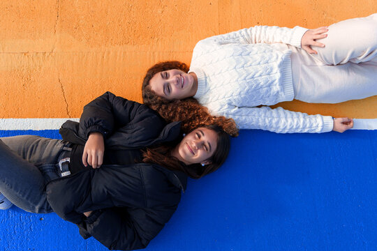 Smiling teenage friends lying on vibrant orange and blue ground, symbolizing youth, diversity, and close connection