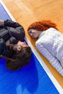 Teenagers lying on colorful ground, looking at each other, enjoying friendship and connection