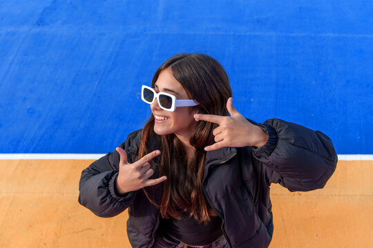 Young woman expressing cool attitude and youth culture with a rock hand sign, smiling with stylish sunglasses