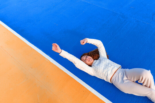 Young woman lying on colorful court stretching, feeling freedom and happiness, enjoying vibrant youth and vitality