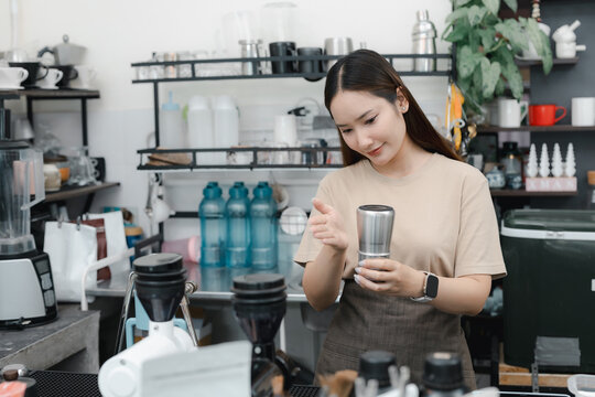 Asian barista holding metal coffee tool behind a cafe counter, preparing espresso in coffee shop with grinders, equipment, small business, hospitality and workplace lifestyle.