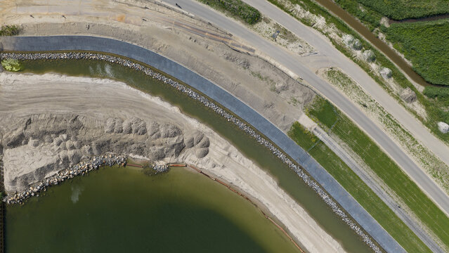 Aerial view of a dike construction site featuring a reinforced embankment, sandy shoreline, and a nearby road in Uitdam, North Holland, Netherlands.
