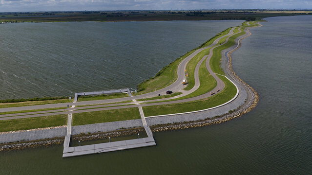 Aerial view of a winding dike road with green grass and a paved path separating the Markermeer lake, featuring a small concrete pier in Uitdam, North Holland, Netherlands.