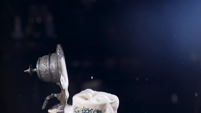 Close-up of beer mug filled with golden beer, ice cube thrown from above causing splashes and flying droplets. Dark background, professional drink videography. Slow motion Full HD video