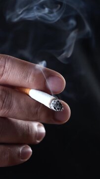 close up man holding smoking a cigarette in hand. smoke spread. dark background.