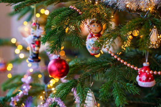 Close-up of Christmas ornament toys and balls hanging on a decorated tree with warm lights, festive tinsel and cozy holiday atmosphere at home.