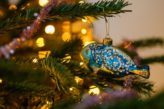 Close-up of Christmas ornament toys and balls hanging on a decorated tree with warm lights, festive tinsel and cozy holiday atmosphere at home.