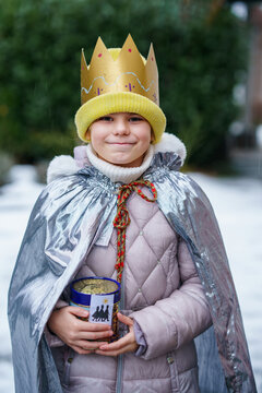 Smiling child dressed as a Sternsinger with crown and silver cape, holding a donation box during the Epiphany tradition in Germany