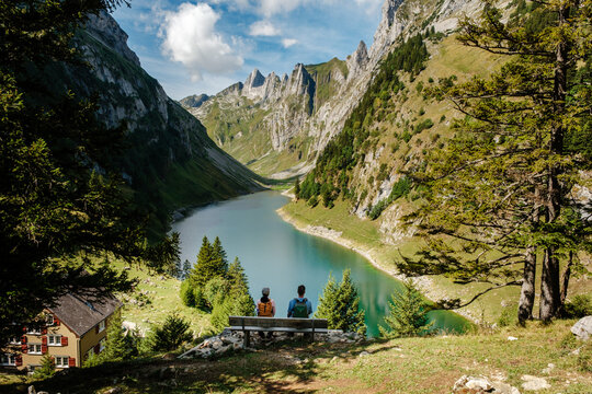 Experience the tranquility of Falensee nestled in Appenzell Switzerland. Hikers enjoy stunning views of the serene lake surrounded by majestic mountains and lush greenery on a bright sunny day.