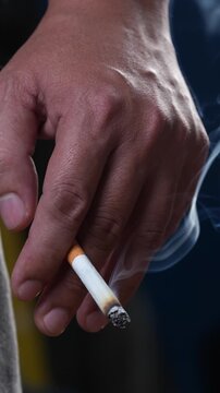 close up man holding smoking a cigarette in hand. smoke spread. dark background.