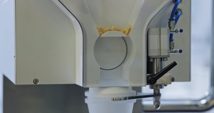 Automated tablet counter doses medicine capsules before packaging on pharmaceutical line. Precision machine measures batch releasing tablets into containers
