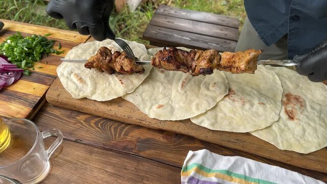 Hot, aromatic pieces of shashlik being slid from the skewer onto lavash bread outdoors. High quality 4k footage