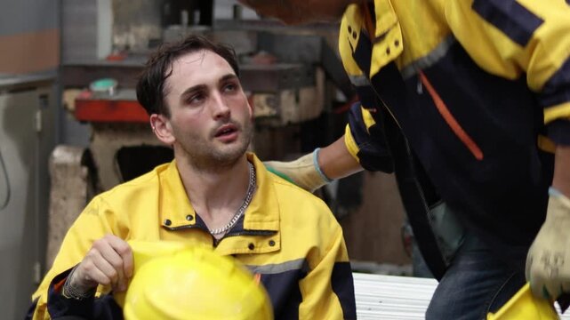 Tired engineer worker in safety clothing take off helmet while rest at industrial manufacturing factory, talk with coworker. Technicians take a break, feel hot and wipe sweat off face after work hard.