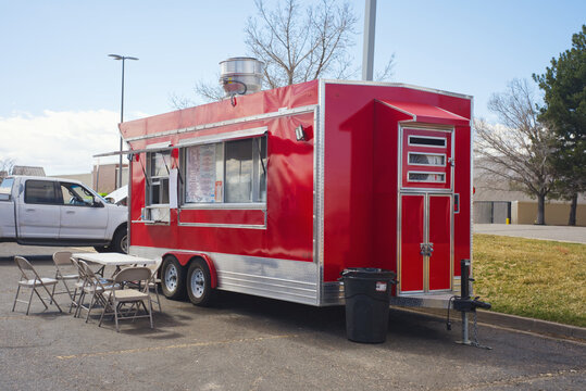 Red food truck parked in a suburban parking lot with folding tables and chairs, serving window and menu board.: USA - March 25, 2025