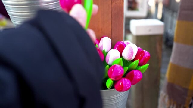 土産物店で木製チューリップの造花を手に取る観光客の手元、オランダの花市場（Hand Picking Up Wooden Tulip Souvenir at a Flower Market Stall in the Netherlands）