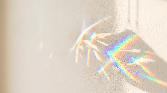 Rainbow light refraction cast by crystal prism on a textured white wall, abstract optical dispersion effect