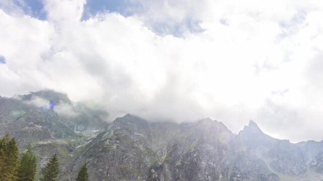View of rugged mountain peaks partially obscured by clouds and evergreen pine trees at Rybie Oko Lake in Chojnice County, Pomeranian Voivodeship, Poland. Timelapse.