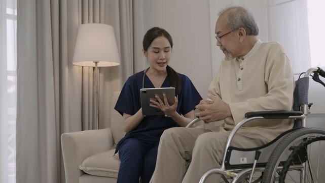 Professional young Asian woman nurse caregiver using a digital tablet to talk and provide advice about healthcare to a senior man patient while sitting in a wheelchair in a special room at hospital. 