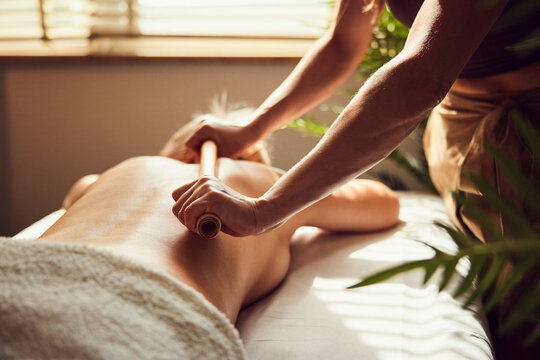 Therapist performing bamboo stick massage on woman at spa