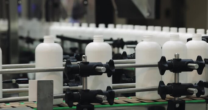 Automated machinery handles row of empty opaque plastic bottles in processing plant. Efficient production systems support large-scale packaging manufacturing