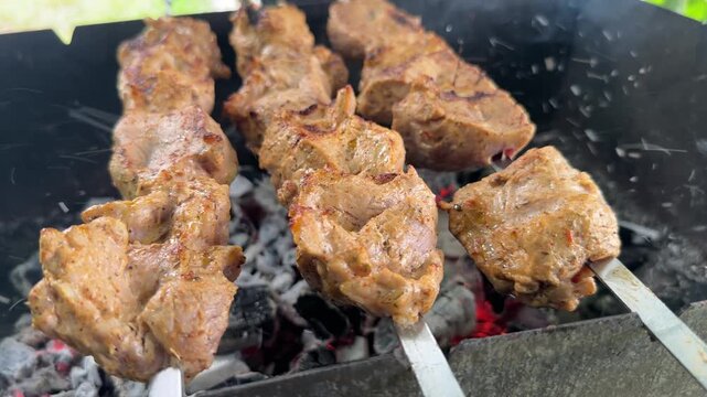 Close-up of meat pieces on skewers grilling over hot coals until a golden-brown crust forms, cooking shashlik outdoors. High quality 4k footage