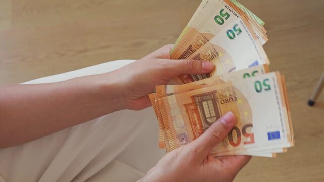 A person sits and counts euro banknotes in their hands. This scene shows the activity of handling money in a relaxed environment.